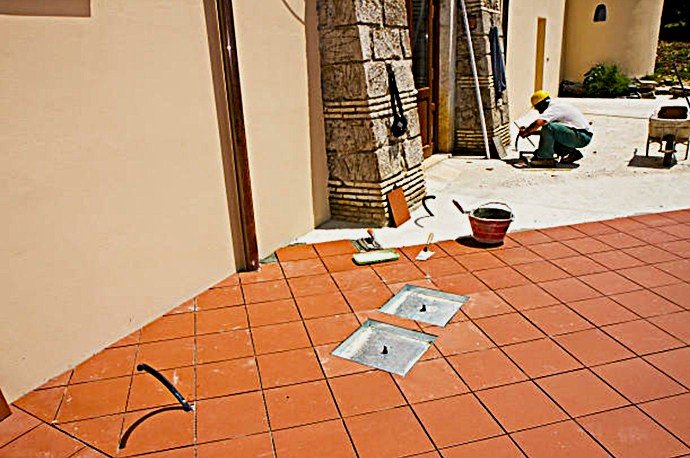 Especialista de obra verificando la nivelación y el fraguado de baldosas de terracota en un proyecto de exterior.